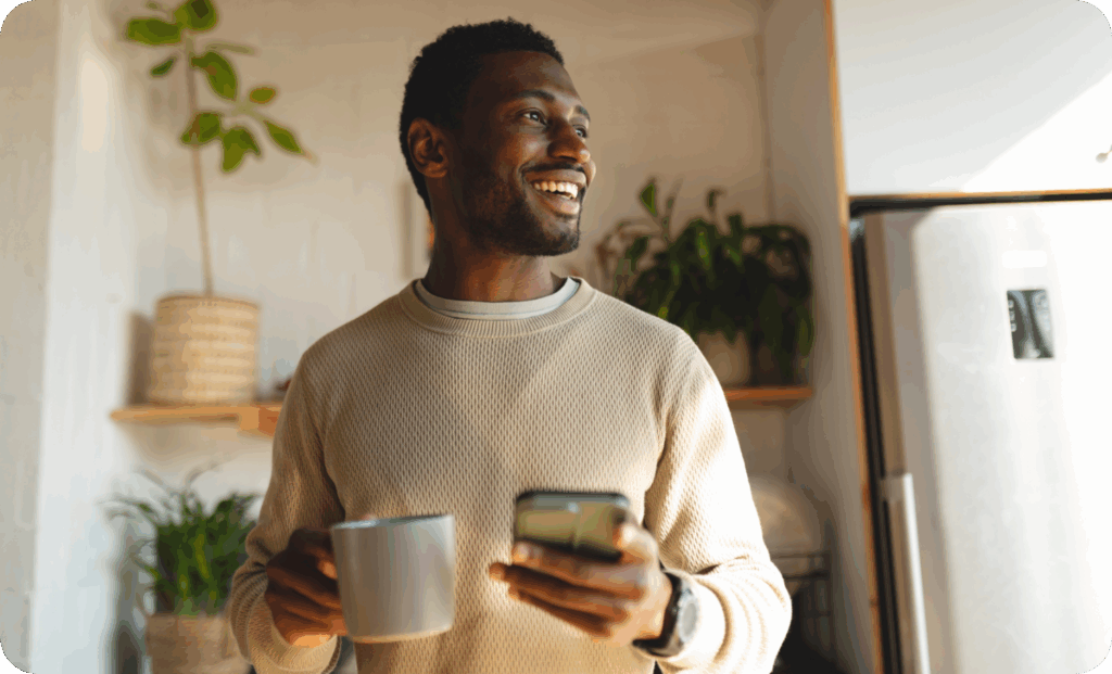 A man standing in a room holding a cup of coffee and a phone
