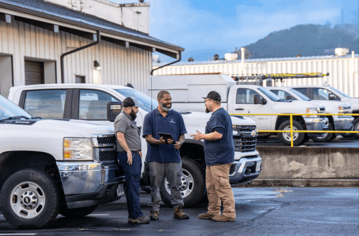 Three men standing in a parking lot in front of some work trucks