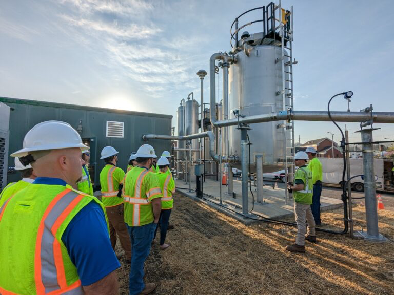 A group of people wearing hardhats and high visibility vests near a gas storage facility.