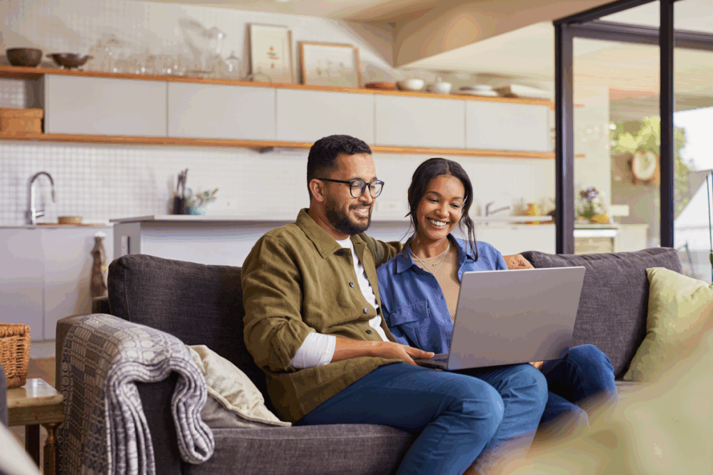 A couple seated on a couch looking at a laptop.