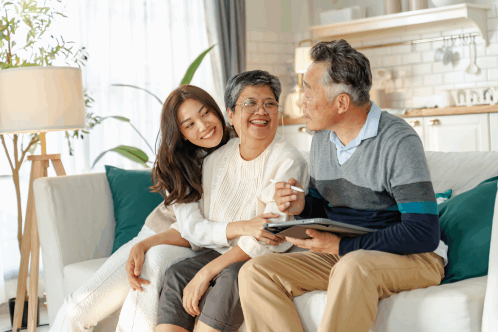 An elderly couple and a young woman seated on a couch. The man holds a tablet and stylus.