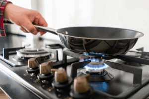 A person holding a frying pan on a lit gas stove burner.