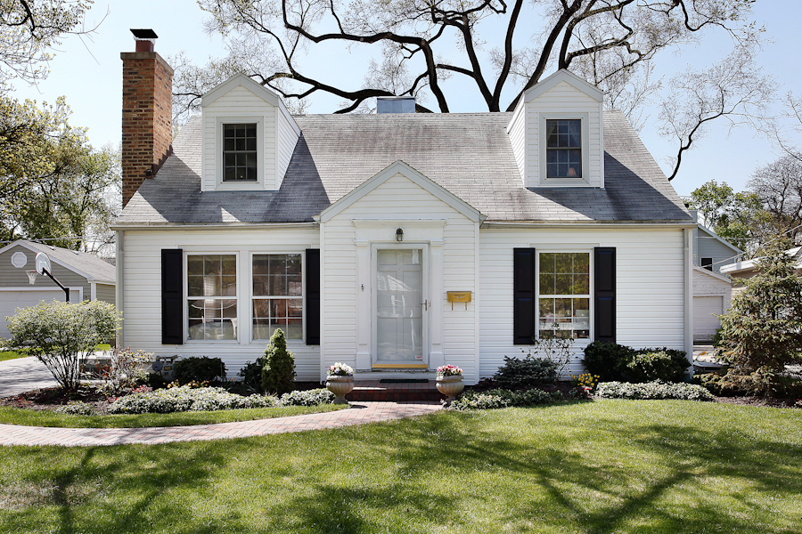 The front of a small white house with dormer windows above it.