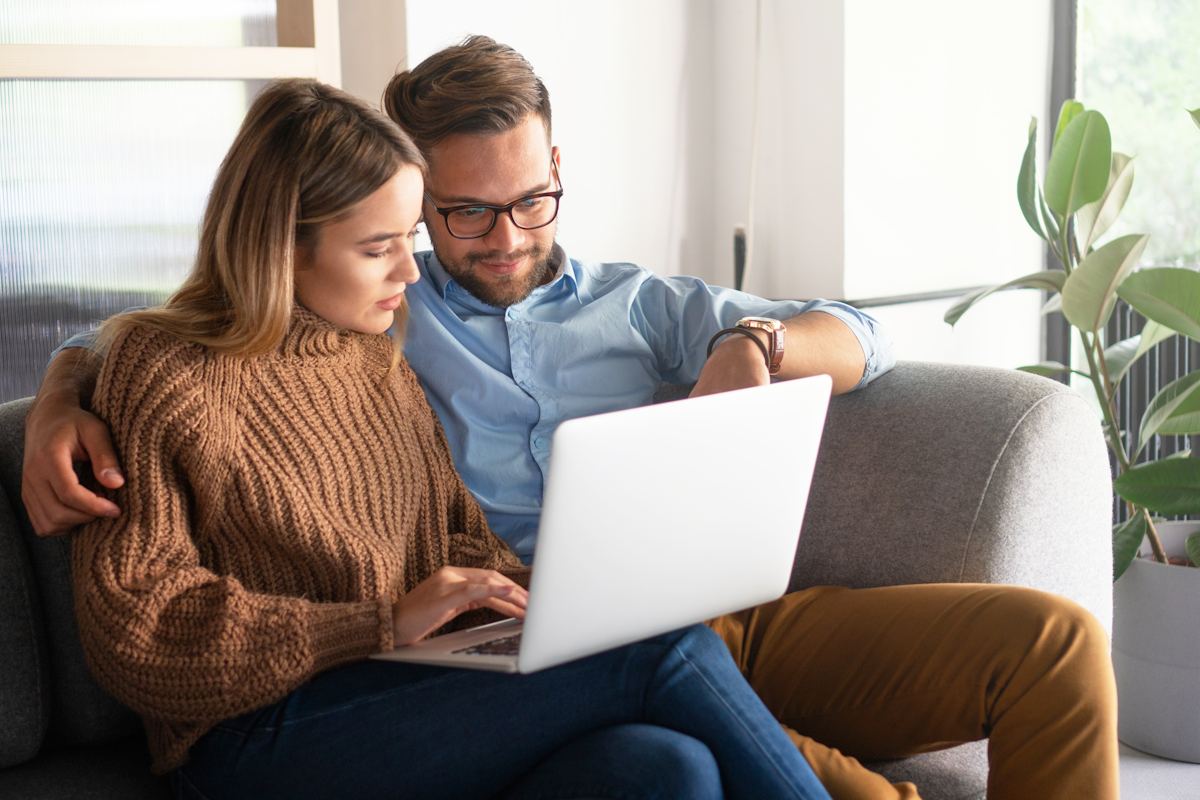 A couple seated on a couch looking at a laptop.