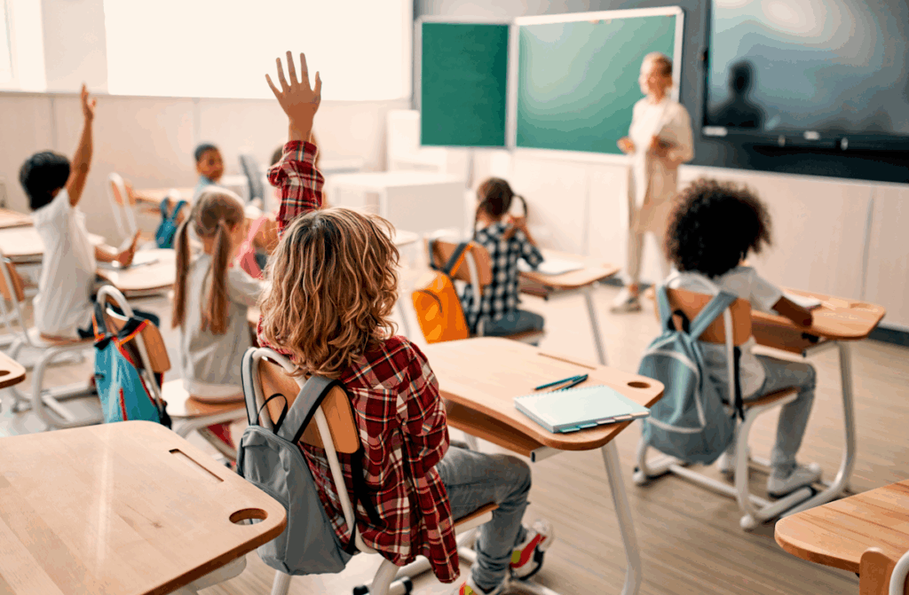 A group of students seated at desks in a classroom with a teacher standing in front of the class.