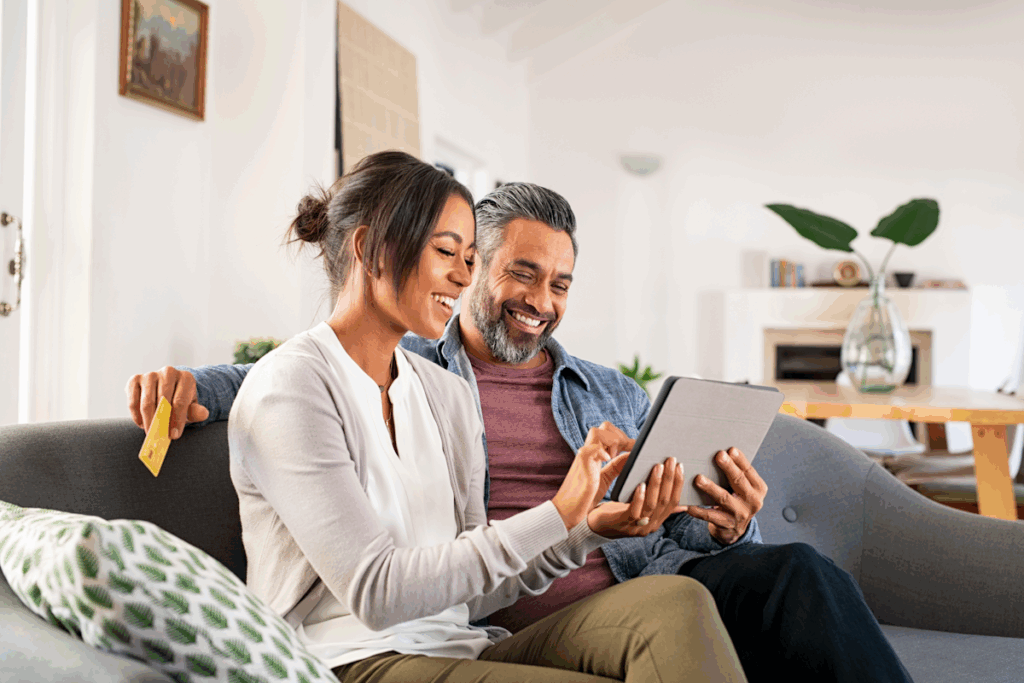 A couple seated on a couch and looking at a tablet.