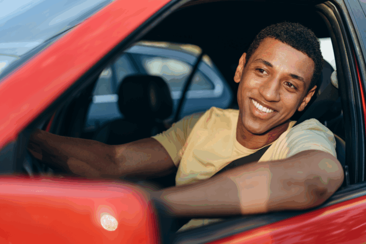 A young man seated in a car looking out his side window.