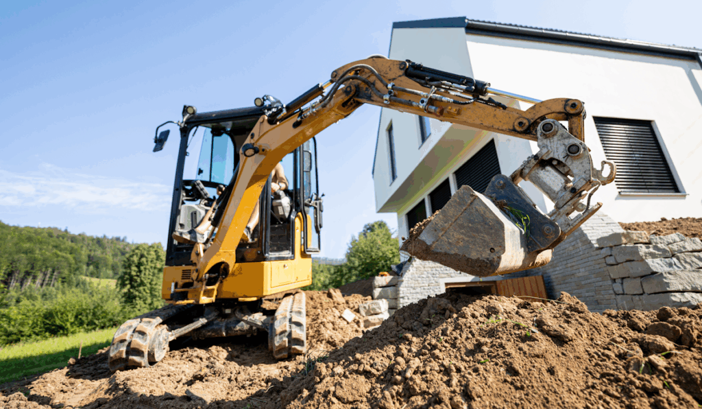 A backhoe digging near the side of a house.