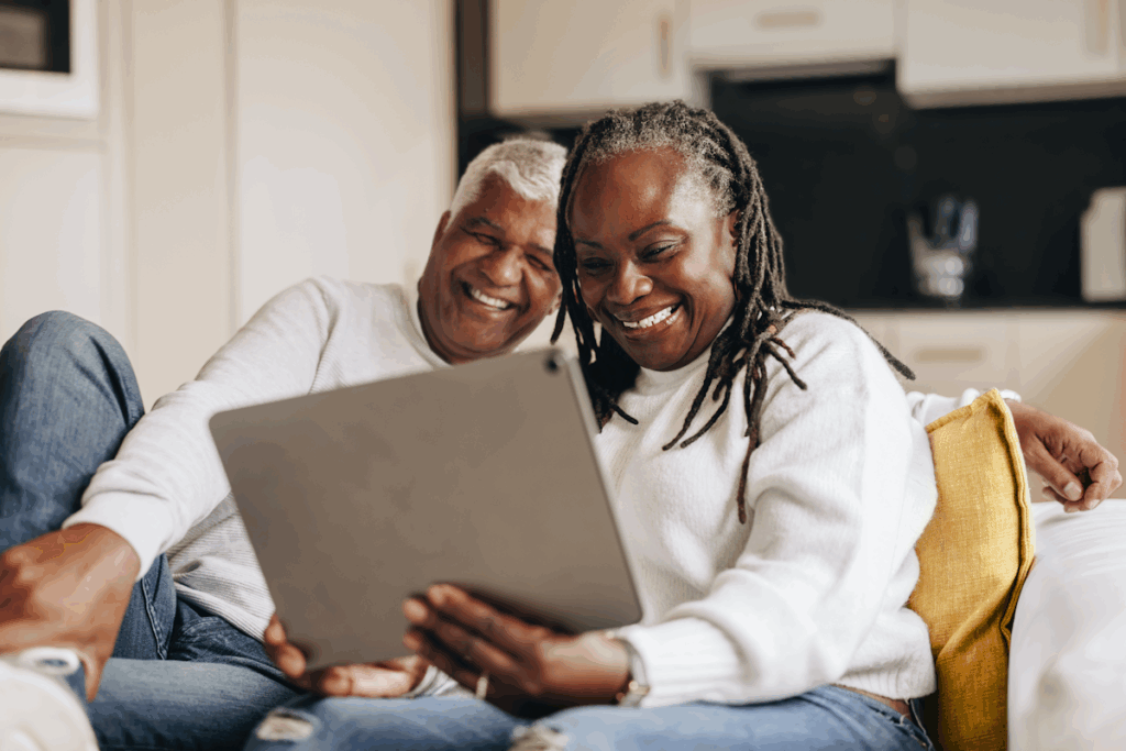An elderly couple seated on a couch looking at a tablet.