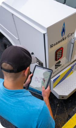A person wearing a ballcap, looking at a tablet, and standing in front of a generator.