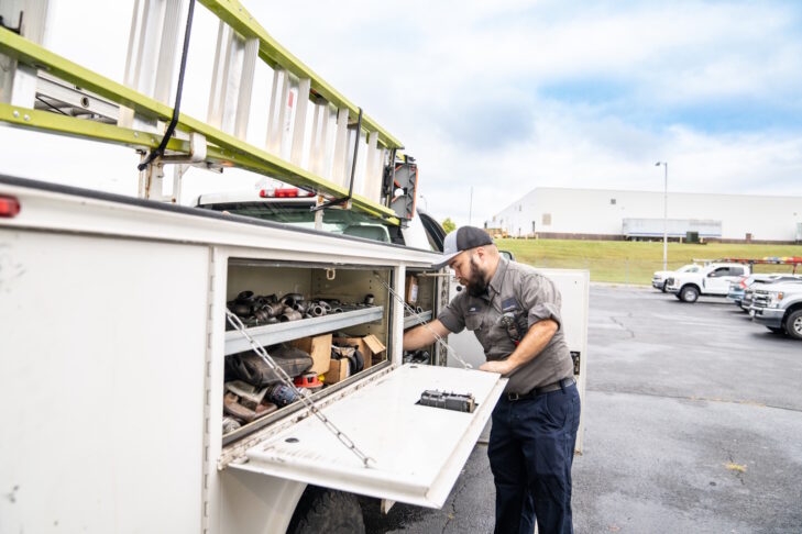 A man standing beside a work truck with the side storage panels open.