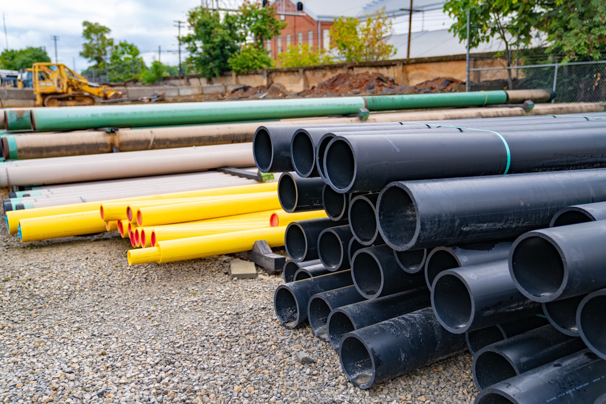 A stack of large pipe sections waiting in a gravel lot.