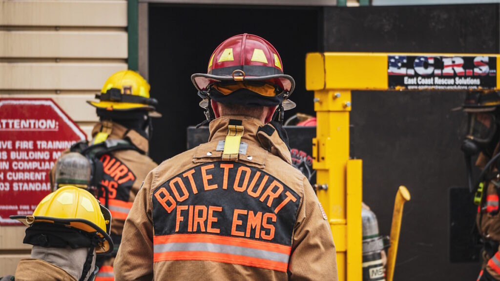 Several fire fighters in protective gear heading into a building.
